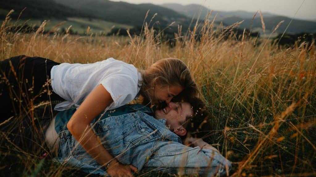 A young couple on a walk in nature in the countryside lying in grass, laughing.