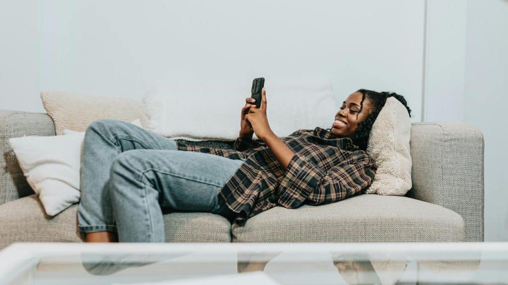 A woman lying on a couch smiling while looking at her phone.