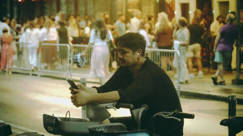 Man on a scooter looking at his phone, surrounded by people in the background.