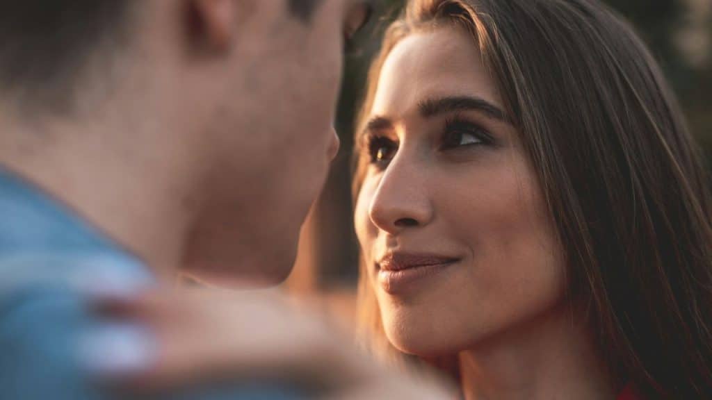 Close-up of a smiling young woman looking up at a man in a blue shirt.