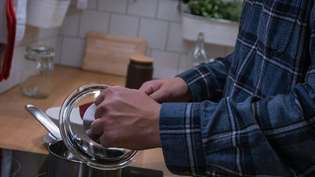 A person in a plaid shirt pouring ingredients into a pot on a stove.