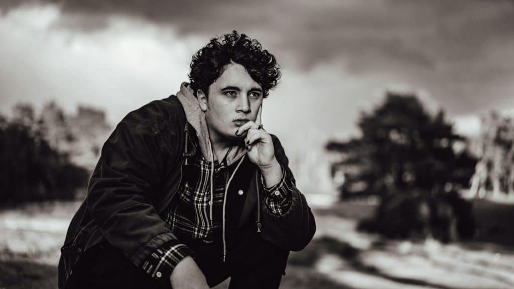 A serious-looking man sitting and thinking with his finger on his cheek.