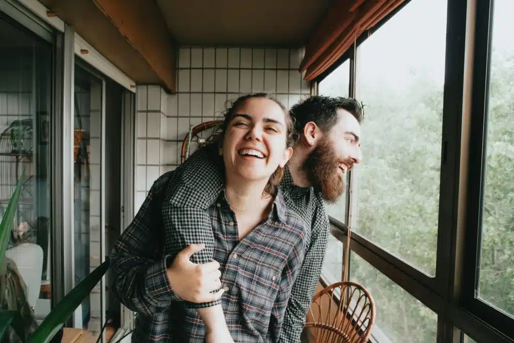 A man puts his arm on a woman’s shoulder, and they laugh together.