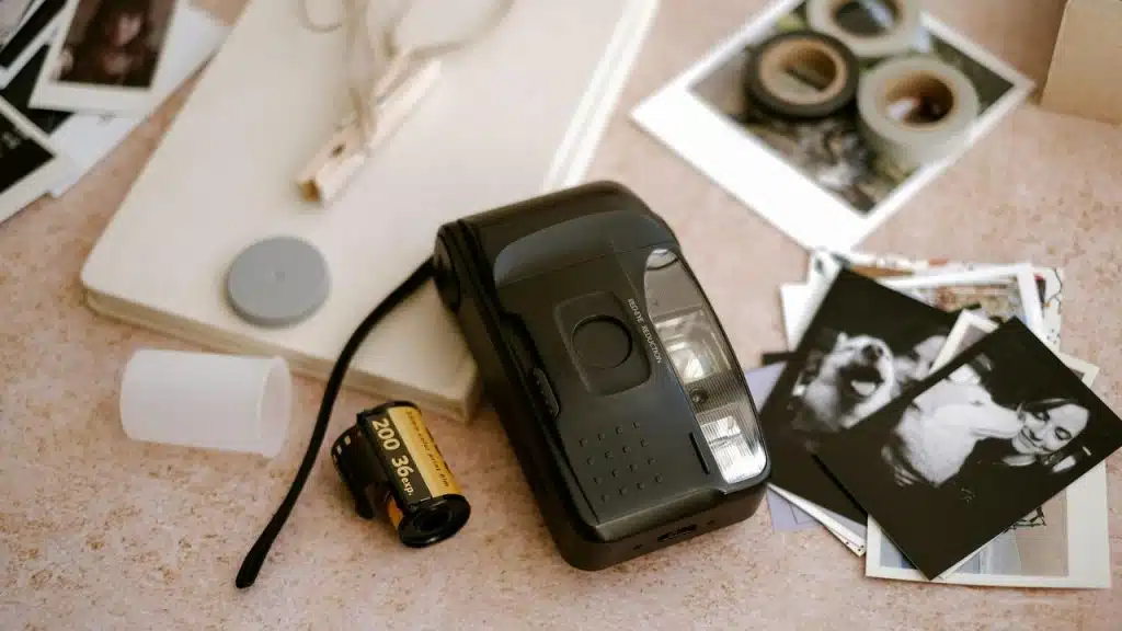 A film camera with a roll of film sits on a table surrounded by printed photographs.