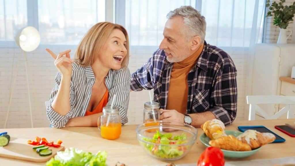 A middle-aged man and woman smile and talk to each other over a table of food.