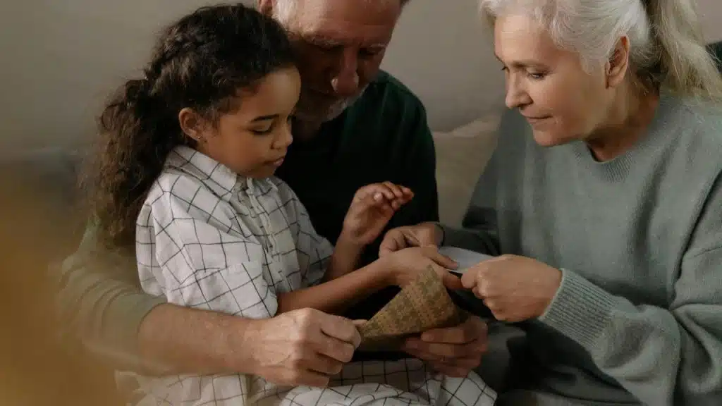 An elderly couple helping a young girl open a gift together.