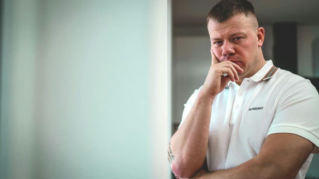 Man with short hair and a white polo shirt, hand on chin, looking at the camera.