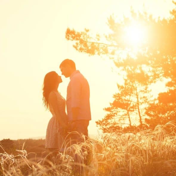 Romantic silhouette of a couple facing each other in a grassy field at sunset.