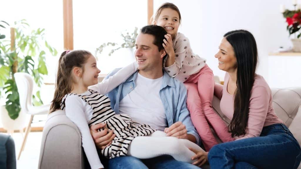Parents sitting on a sofa with their little daughters.