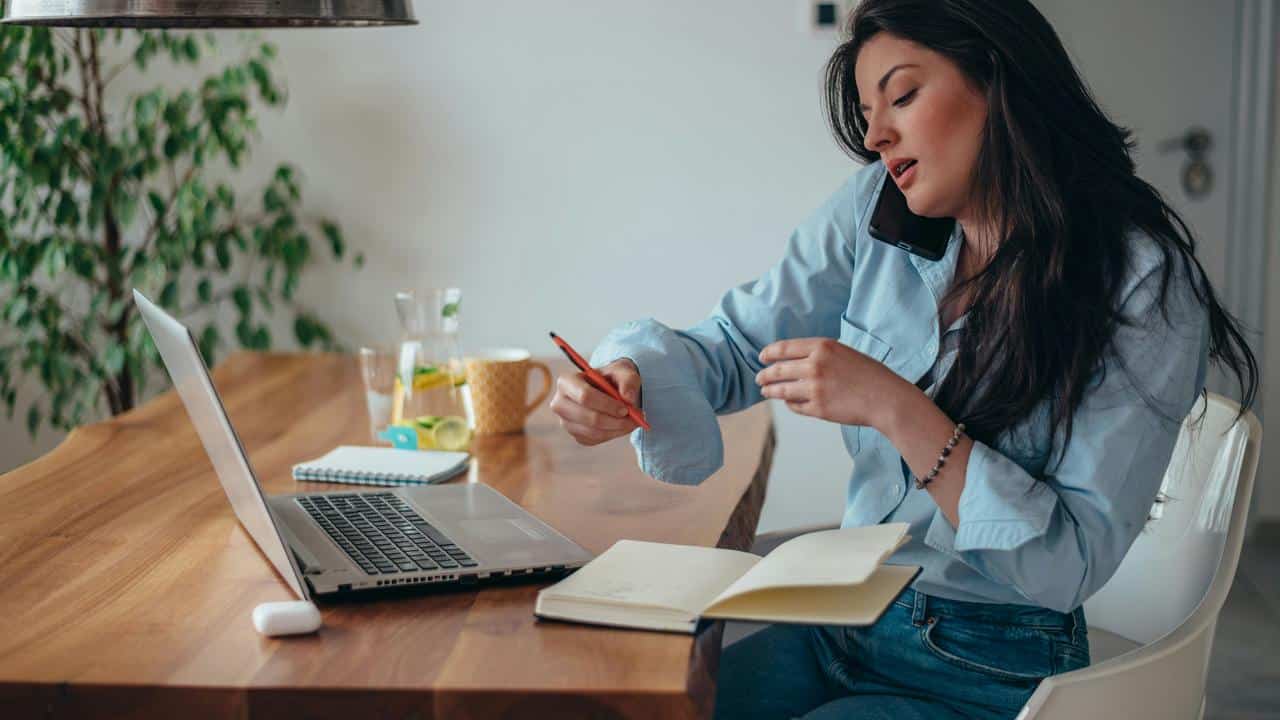 A woman multitasking with a phone on her shoulder while working on a laptop.