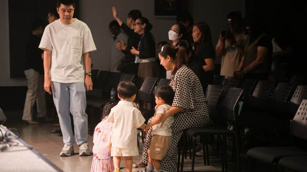 A man stands solemnly as a woman tends to three small children in a dimly lit room.