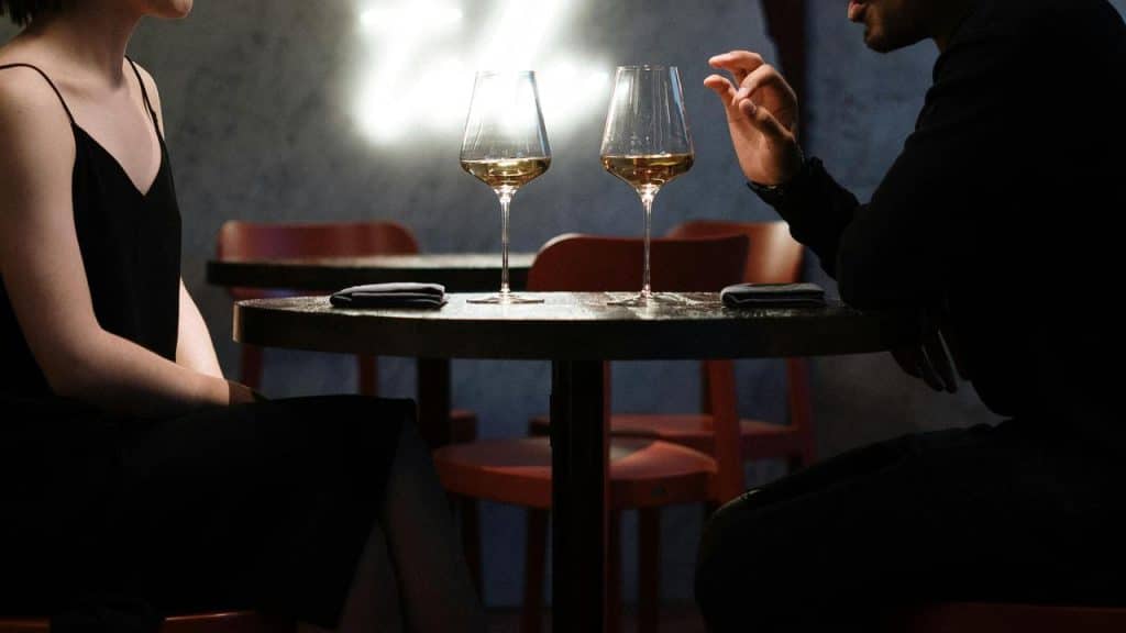 A man and woman sitting at a small table with two glasses of wine.