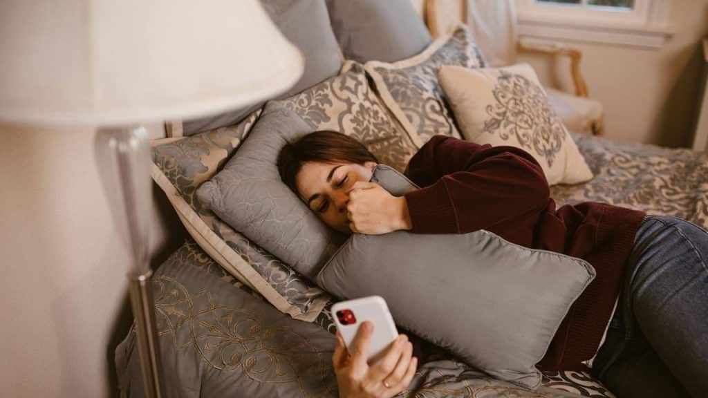 A woman lying on a bed holding a pillow and looking at her smartphone.