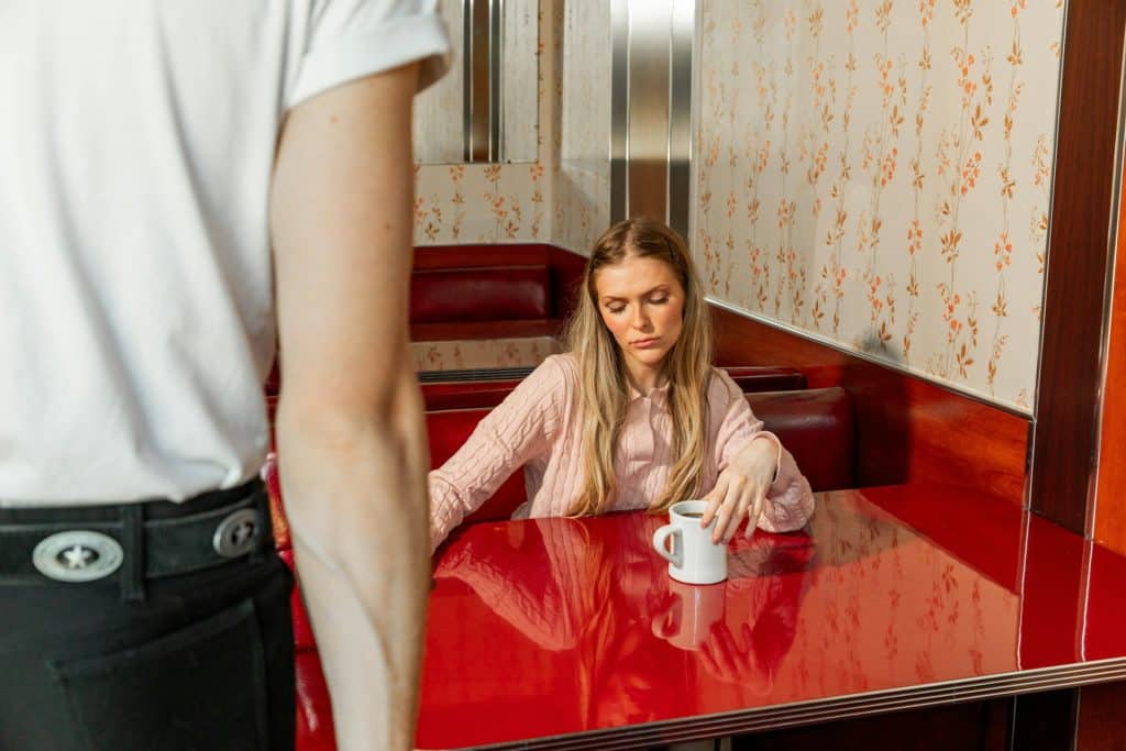 A frowning woman sits at a table in a diner.