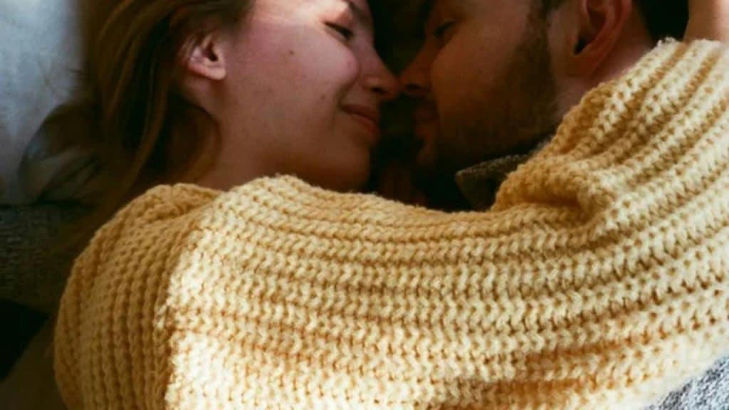 A couple lies close together, embracing warmly and smiling.