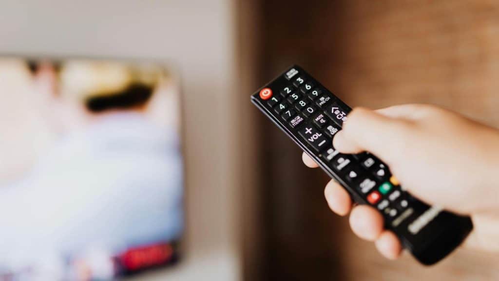 A person’s hand holding a TV remote while pointing it at a screen.