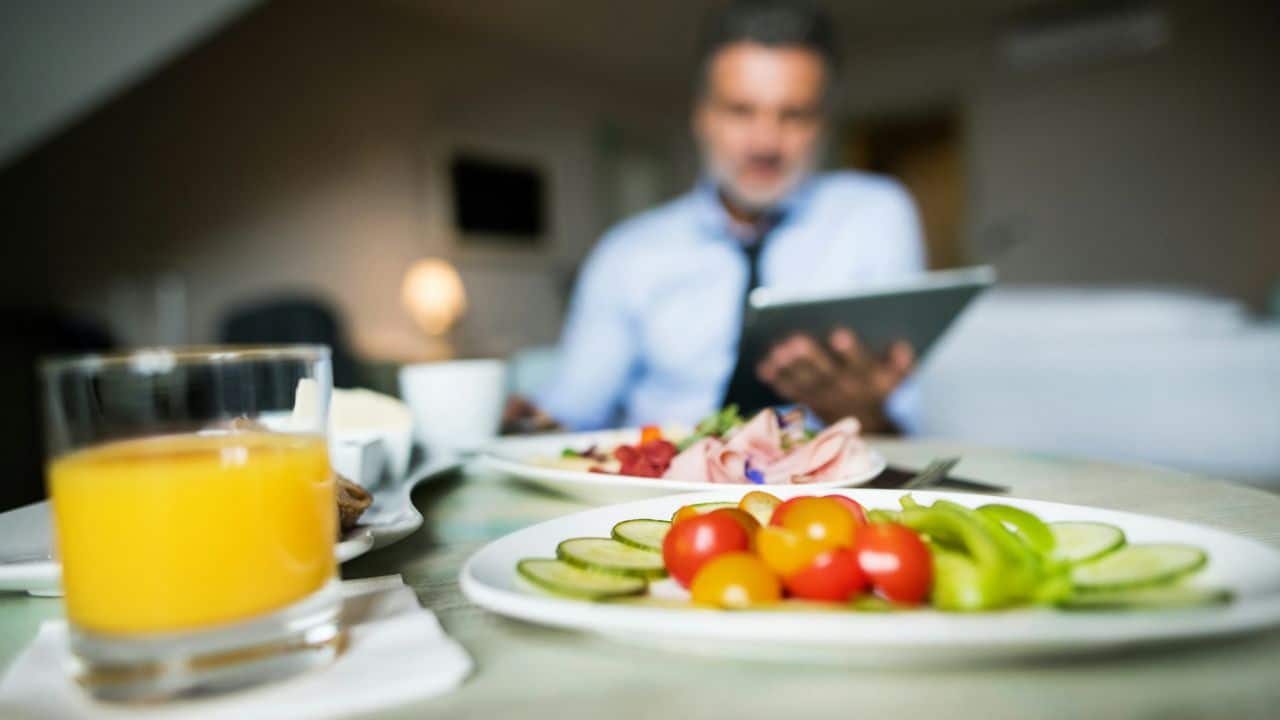 A plate of sliced vegetables is on a table with a man reading a tablet in the background.