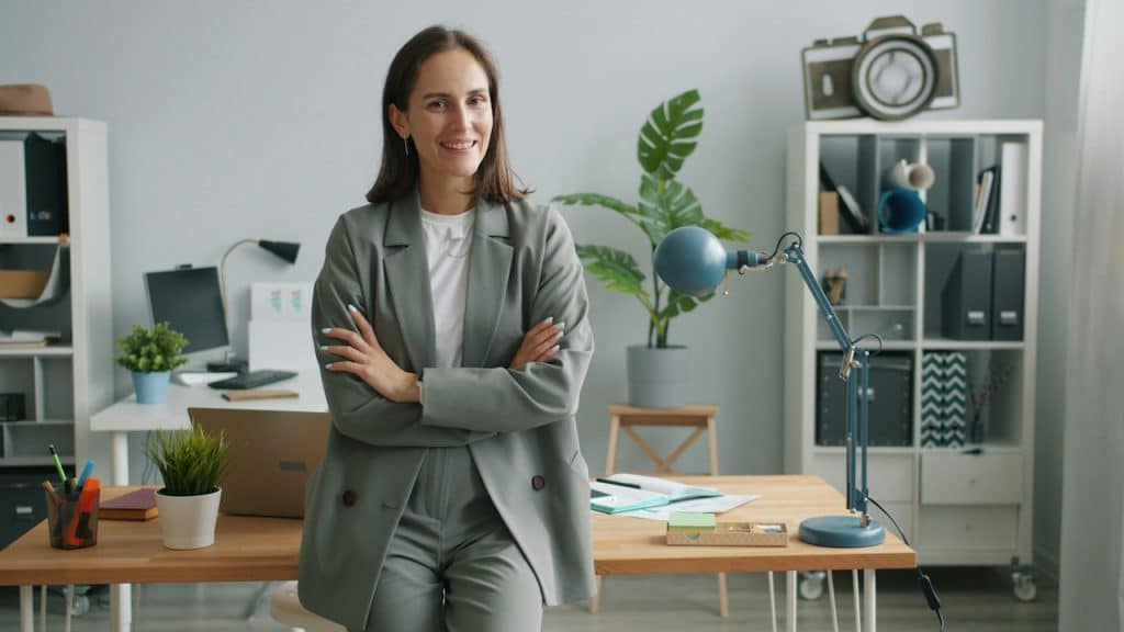 A woman wearing a gray suit standing in an office with her arms crossed.