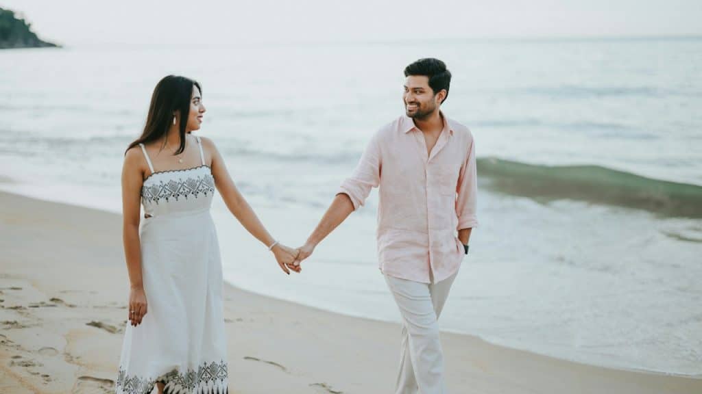 A couple holding hands walking on a beach.