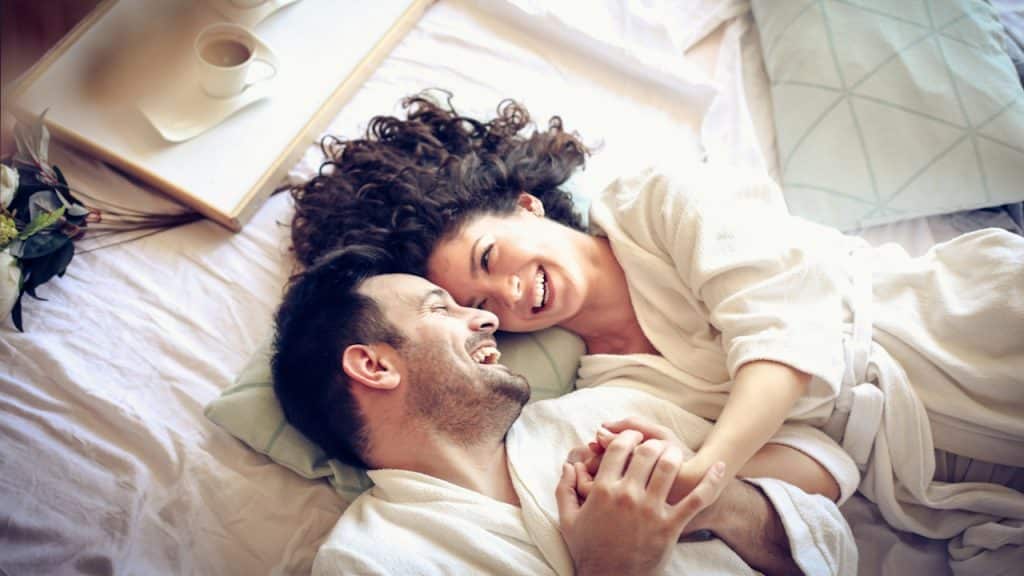 A happy couple in bed laughing and hugging each other.