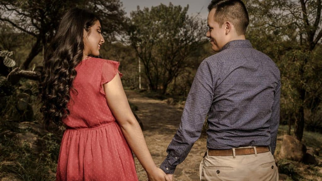 A couple walking hand in hand down a wooded path.