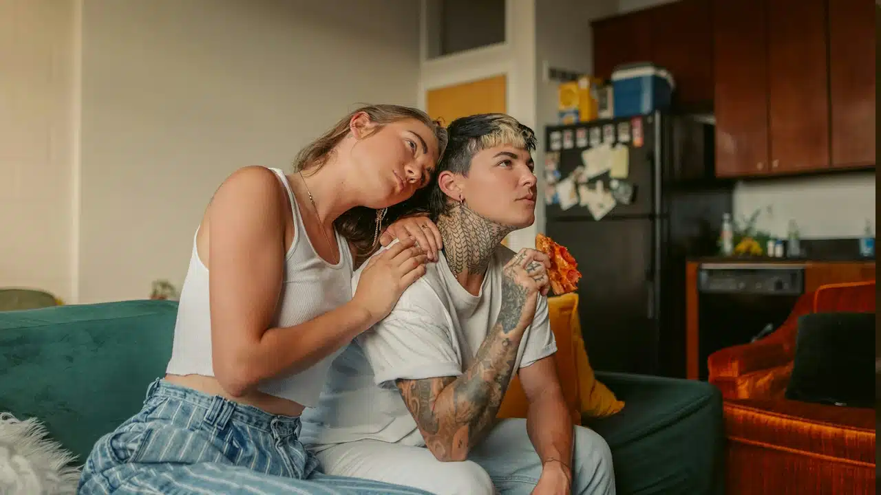 A man and a woman eating pizza and watching television together.