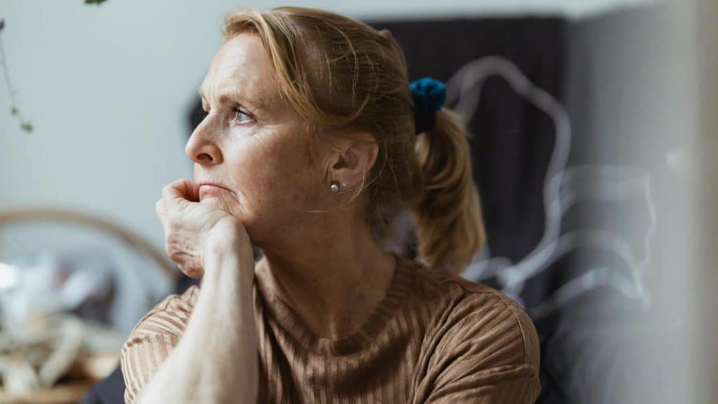 An older woman resting her chin on her hand and looking thoughtfully to the side.
