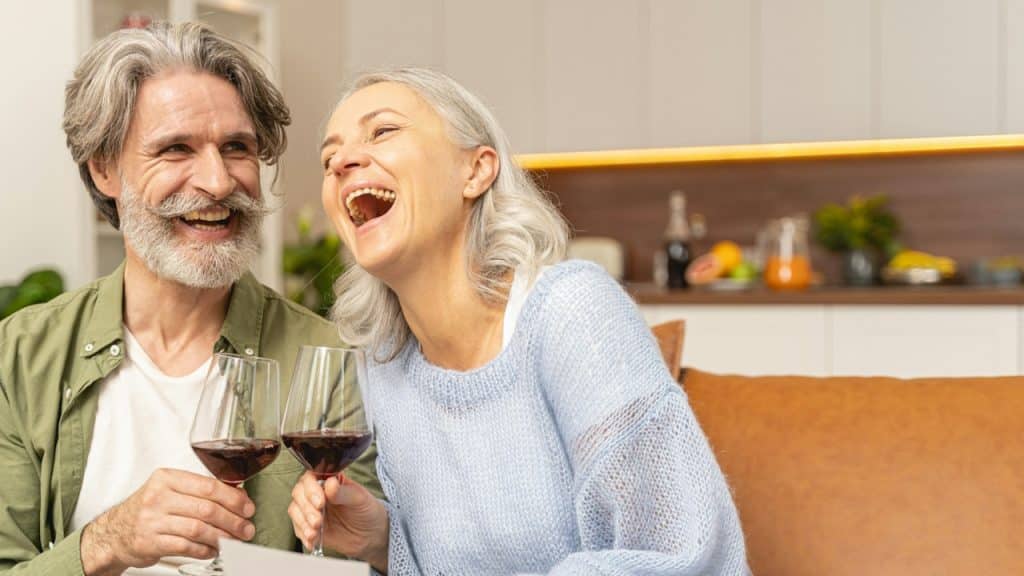A couple laughing together while holding glasses of wine.