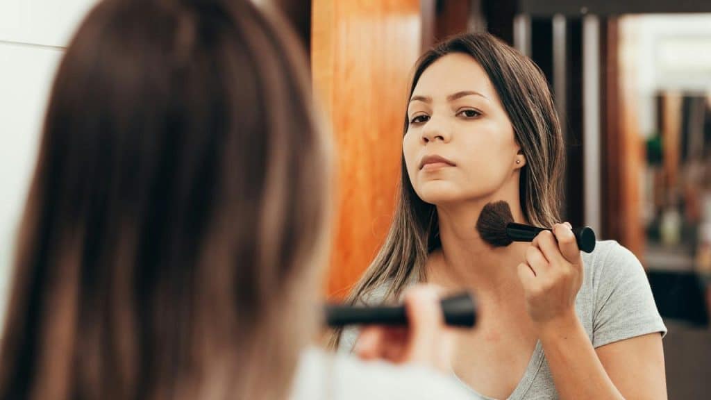 A woman applying makeup while looking in the mirror.
