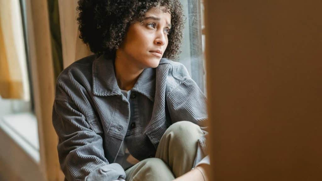 A woman sitting by a window looking outside thoughtfully.