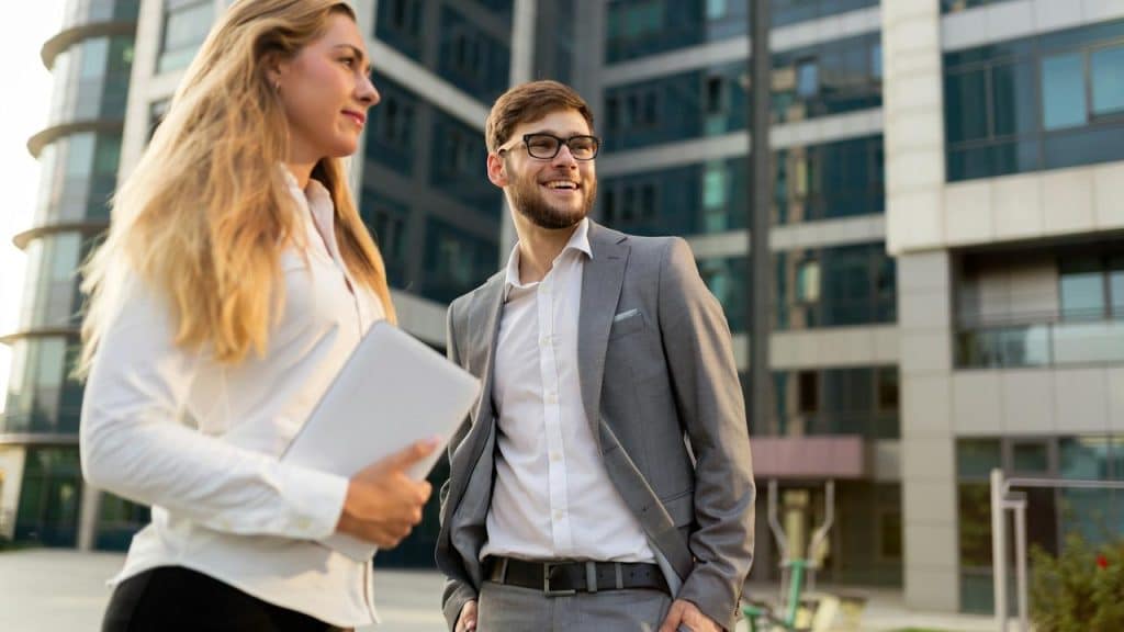 A man in a suit and a woman holding a tablet standing outside an office building.