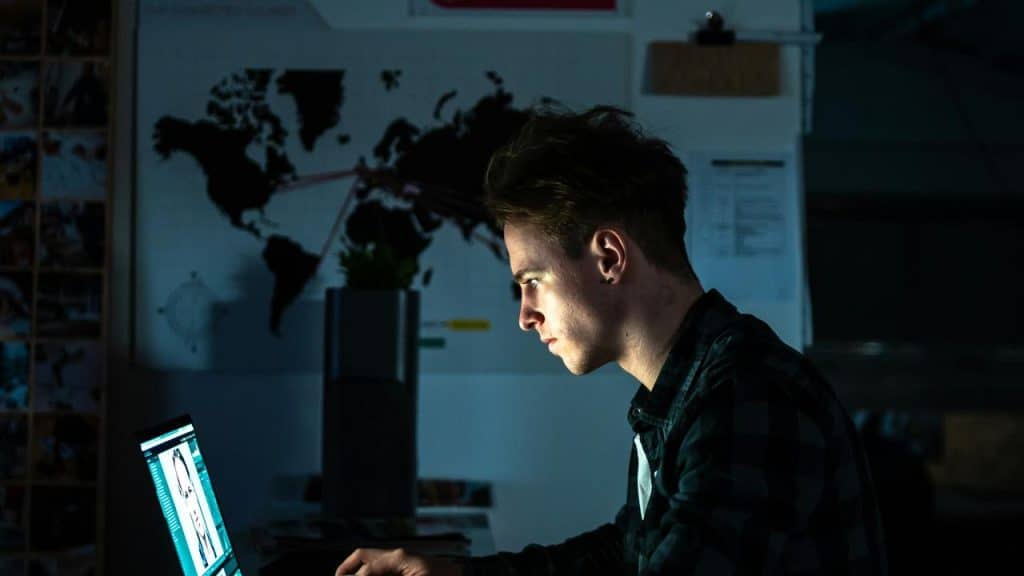 A man working on a laptop in a dimly lit room.