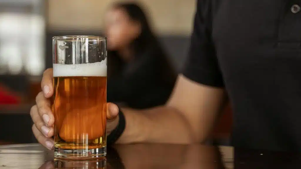 A person holding a glass of beer at a table.