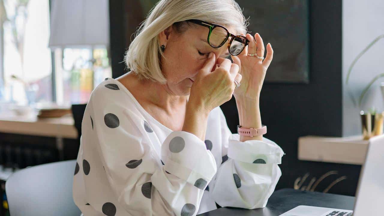 An older woman rubbing her eyes in tiredness at a desk.