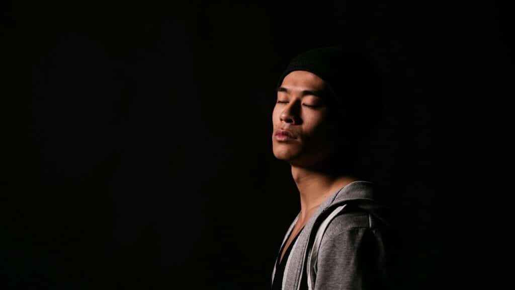 A man standing in the dark with his eyes closed.
