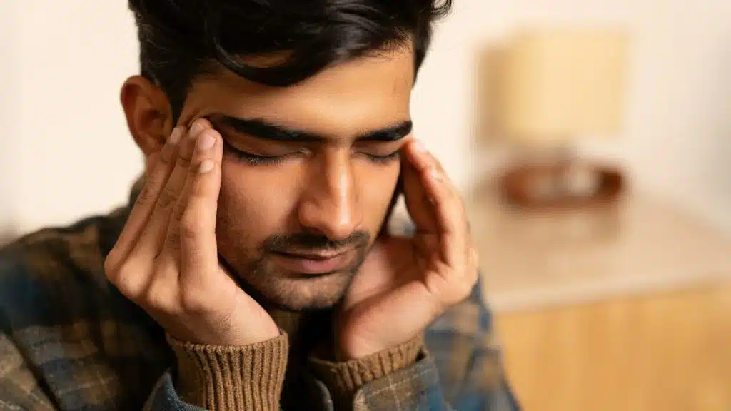A man with eyes closed is pressing his temples with his fingers, appearing stressed.