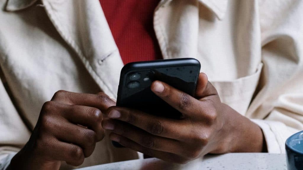 A person in a beige coat uses a smartphone at a table.