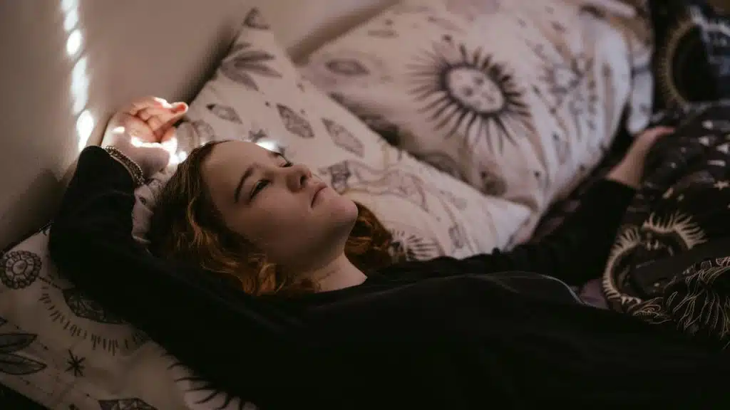 A woman lies in bed staring upward with a thoughtful expression.