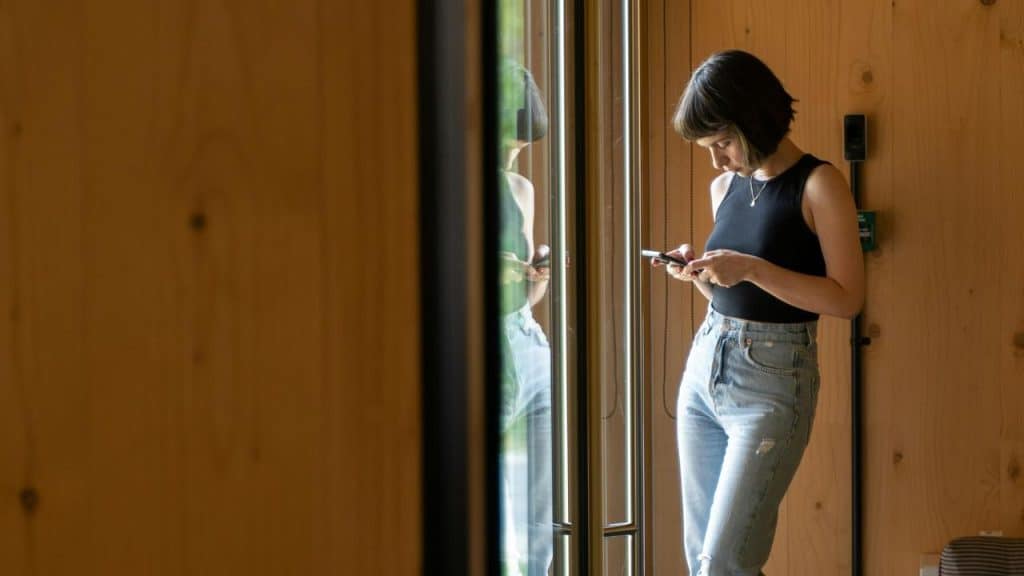 A woman standing by a glass door using her smartphone.