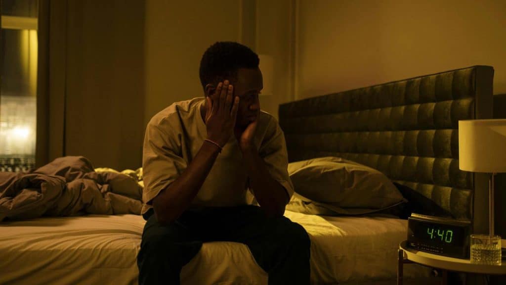 A man sitting on a bed at night with his hands on his face, looking tired.