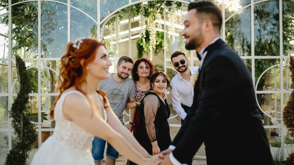 A bride and groom hold hands while friends smile and pose behind them.