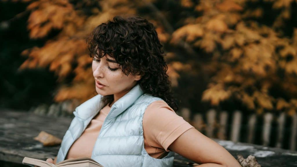 A woman reading a book outdoors in autumn.