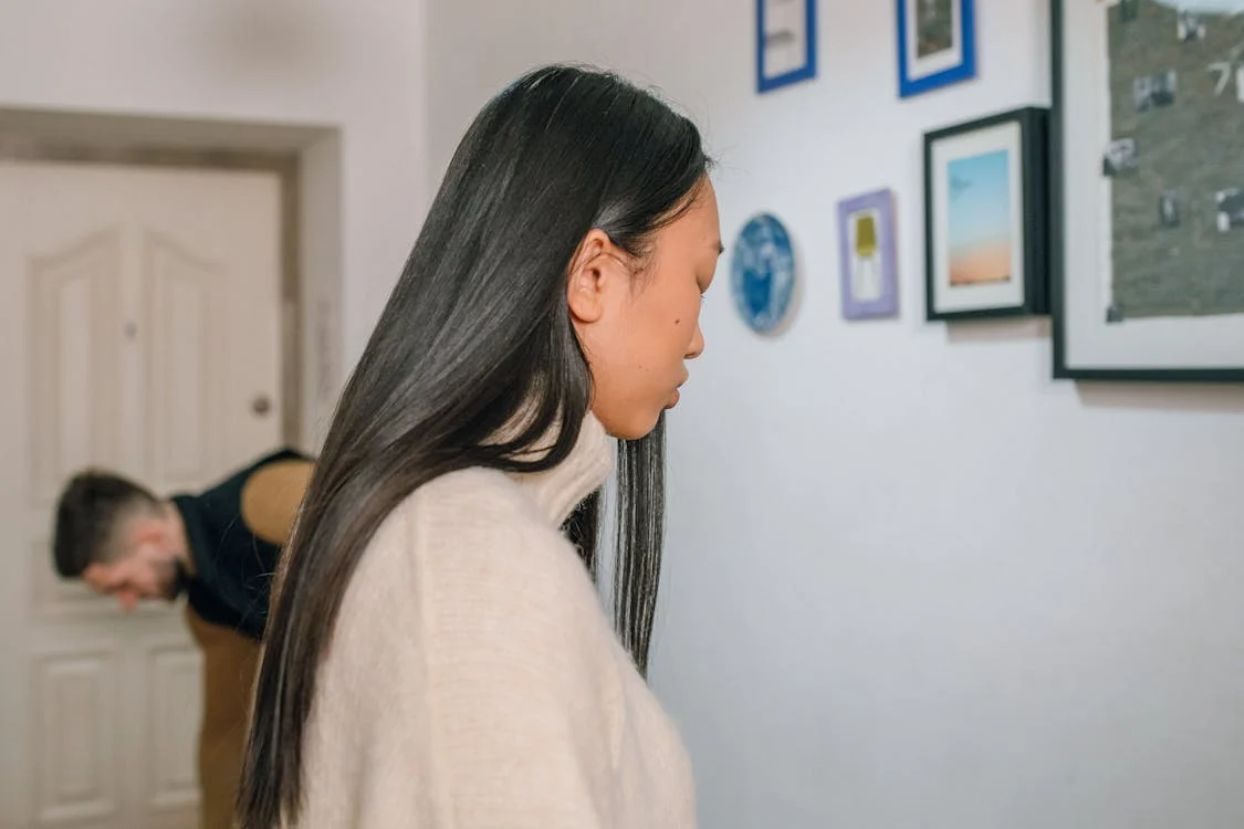 Upset woman standing in the hallway in an apartment with a man dressing to go out