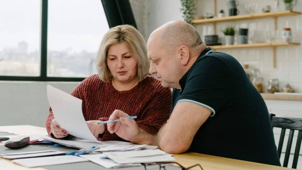 Two middle-aged people reviewing documents at a table indoors.