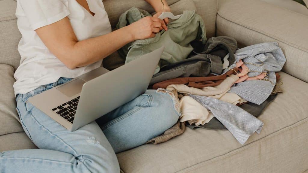 A person working on a laptop while sorting out clothes.