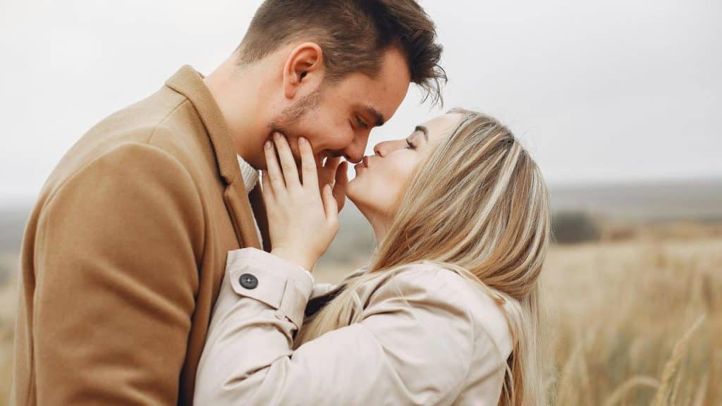 A couple standing on a grassy field and appearing to kiss each other.