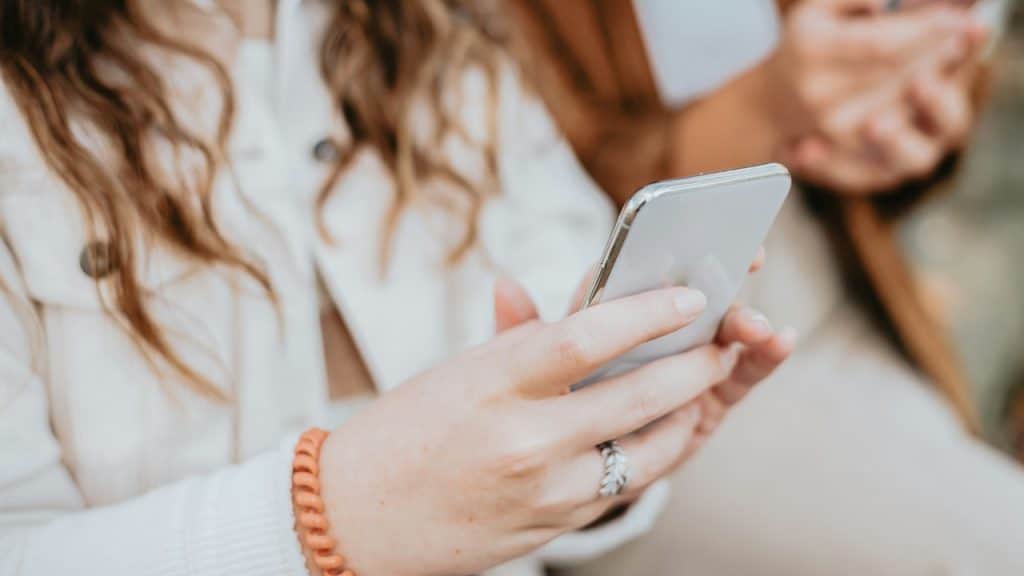A close-up of a person's hands holding a silver smartphone and texting.