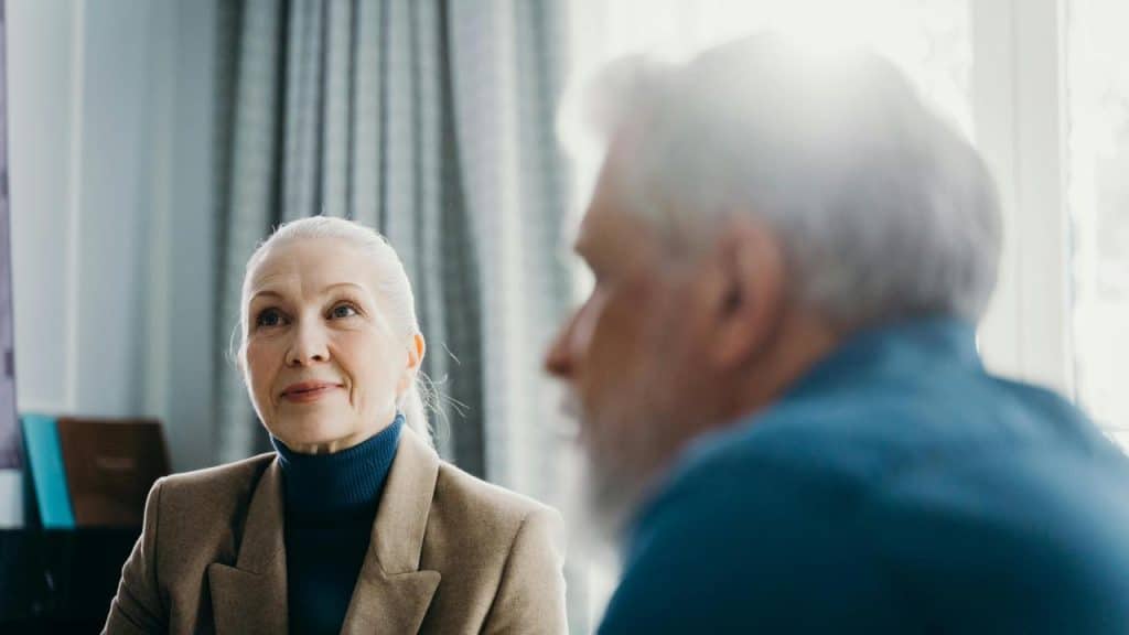 An older woman smiling as she listens to a man in a softly lit room.