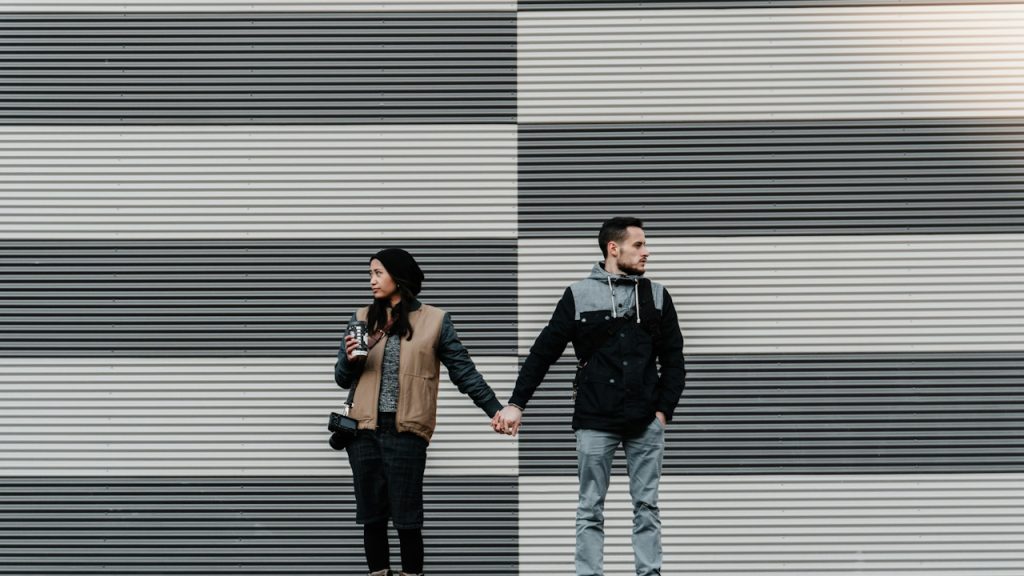 A couple holding hands and looking in opposite directions.