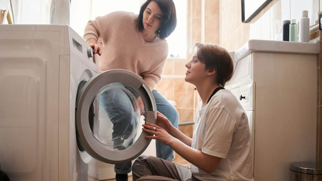 Two women working together to operate or examine a front-loading washing machine.